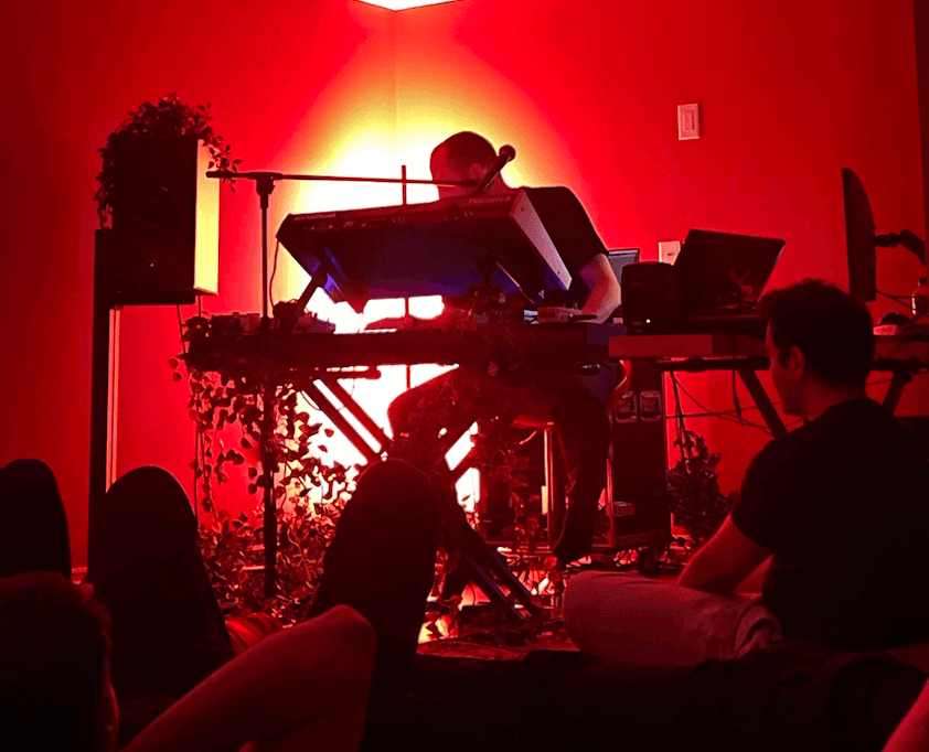 Tim Penner performing the multichannel immersive show in red ambient light, audience seated around the room