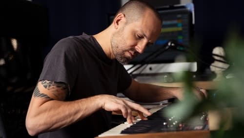 Tim Penner playing keys in his studio, hands on keyboard, focused down at the keys