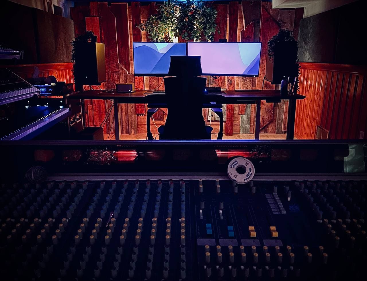 Tim Penner's studio — mixing console foreground, monitors and synth left, wood-paneled wall